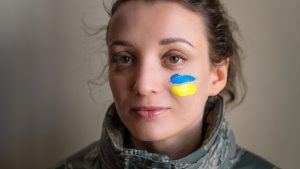 Luciana Scrofani Green Indoor portrait of young girl with blue and yellow ukrainian flag on her cheek wearing military uniform, mandatory conscription in Ukraine, equality concepts.
