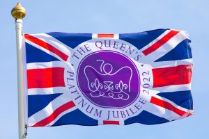 Luciana Scrofani Green interpreting Norfolk, UK - April 8th 2022: A flag commemorating the Queens Platinum Jubilee 2022, flying over a clear blue sky.