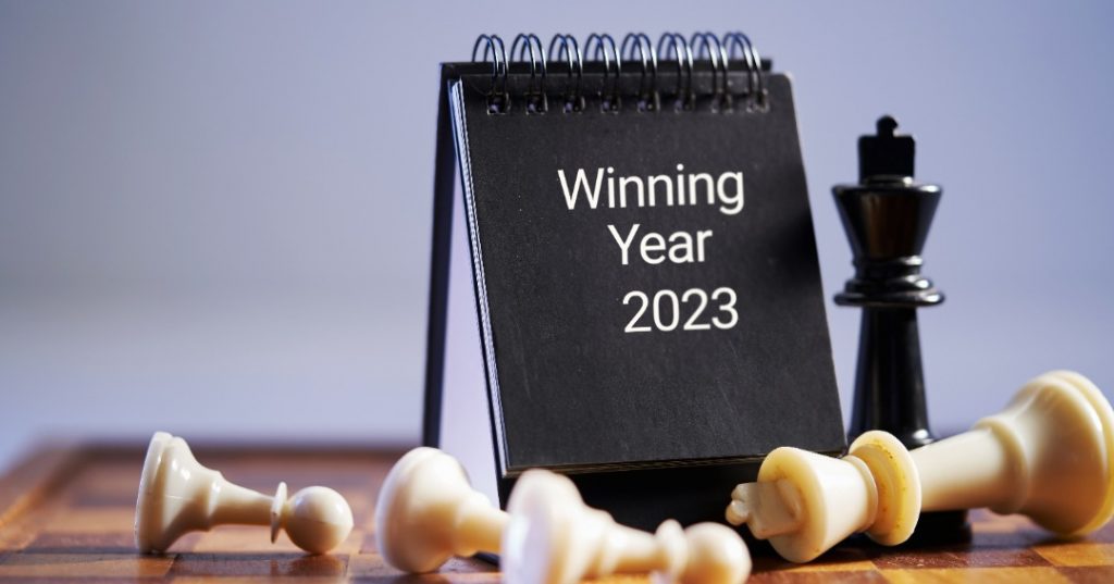 Front of a black desk calendar with Winning Year 2023 in white font surrounded by white and black chess pieces