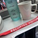 Red escorted visitor lanyard in front of a water bottle and mug