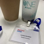 Name badge with blue lanyard in front of a disposable coffee cup and water bottle