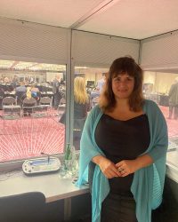 Luciana in a black dress with aqua shawl in a interpretation booth for a World Bank Geneva event